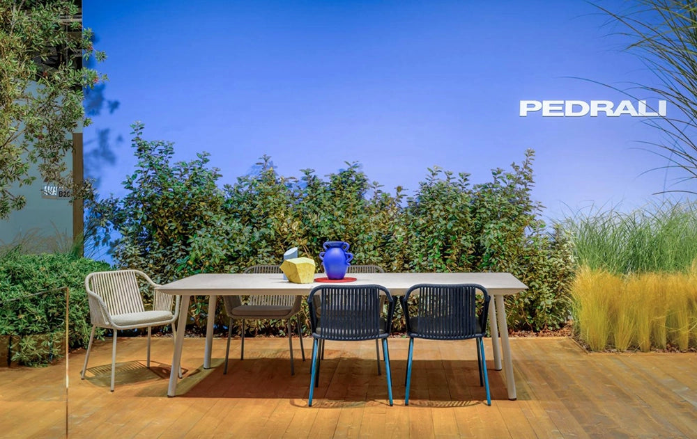 Babila Twist Dining Chair with Armrests in Grey Finish with Green Plants and White Table in Outdoor Setting