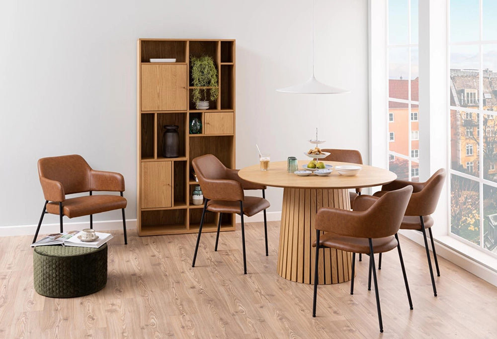 Hilda Round Dining Table in Matte Oak Finish with Pouf and Armchair in Breakout Setting