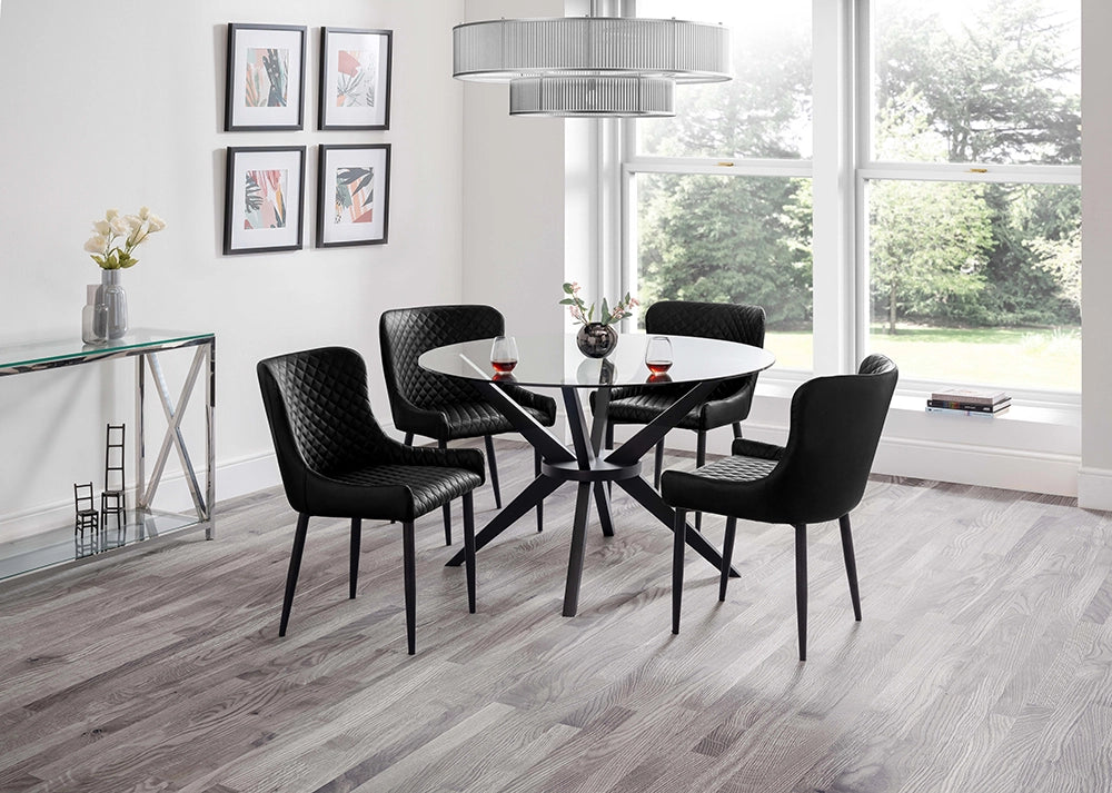 Jayden Round Dining Table in Glass Top with Padded Black Chairs and Tansparent Vase in Breakout Setting 2