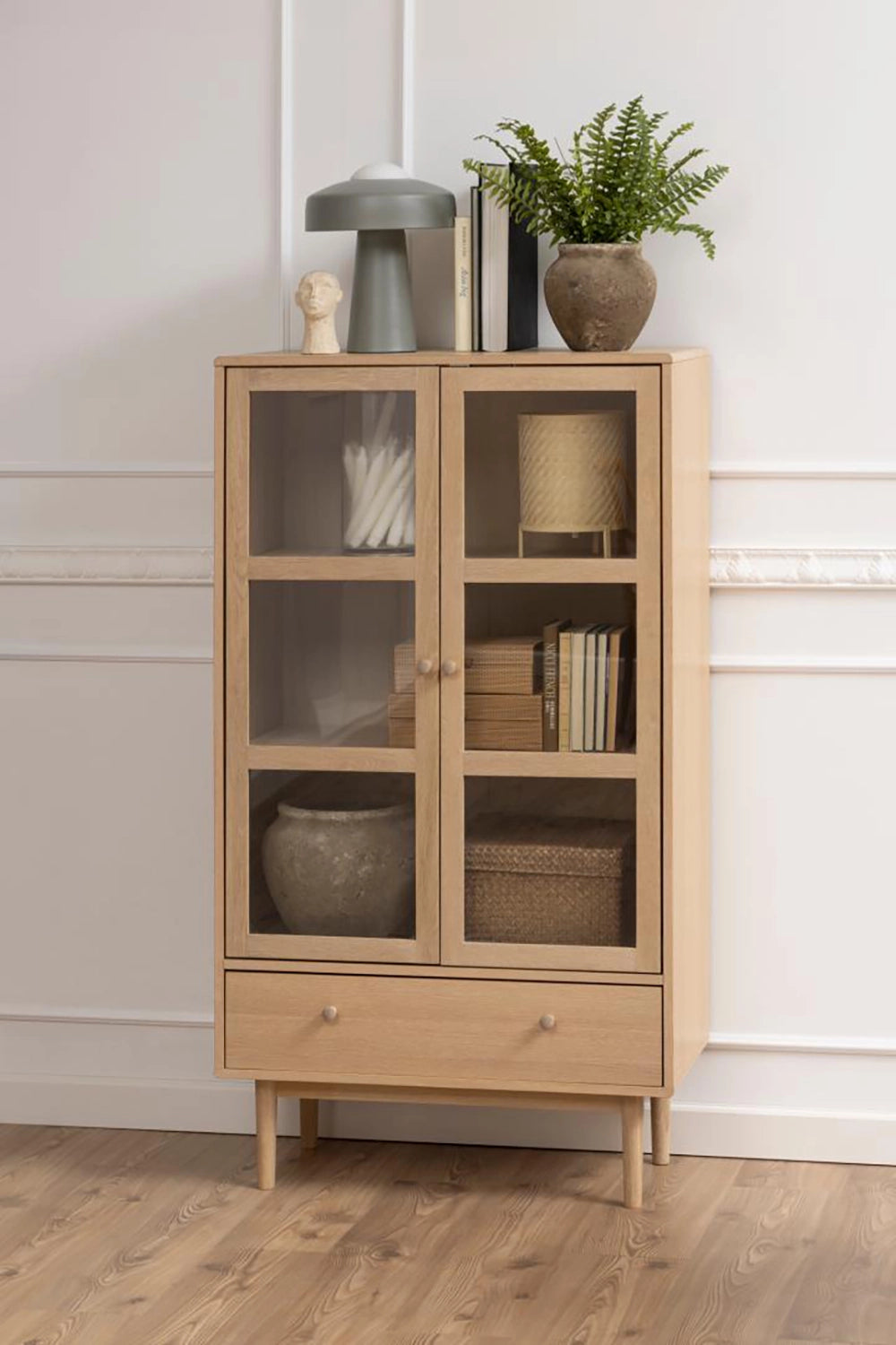 Krutcher Display Cabinet in White Oak Finish with Clay Plant Pot and Books Inside in Living Room Setting