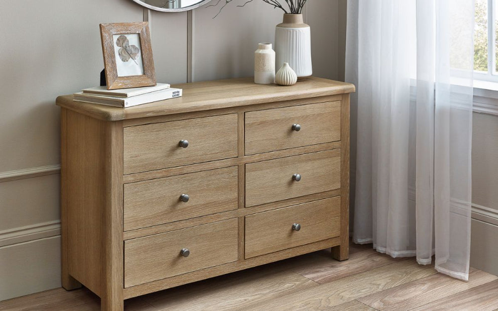 Marissa 6 Drawer Wide Chest in Limed Oak Finish with Flower Vase and Books in Bedroom Setting