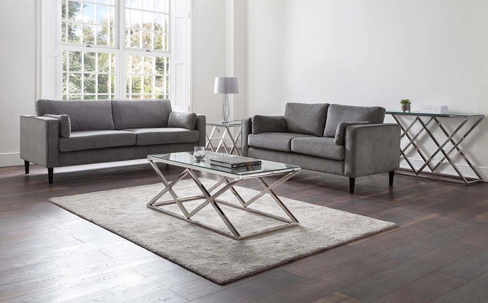 Ritz Glass Top Coffee Table with White Table Lamp and Upholstered Grey Sofa in Living Room Setting