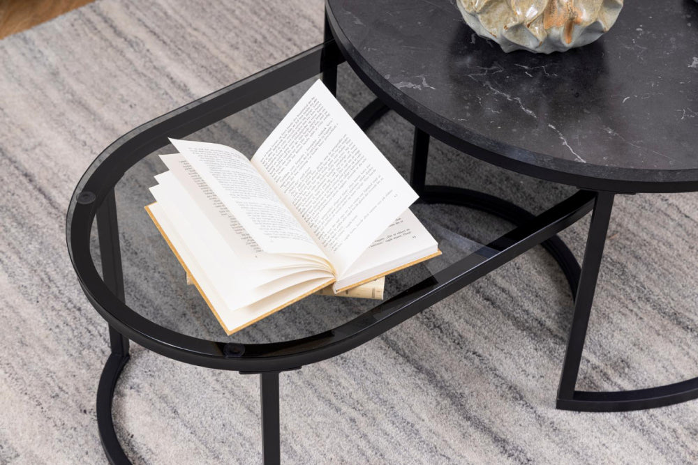 Riva Oval Round Coffee Table Smoked Glass Black Marble with Book and Carpet in Living Room Setting